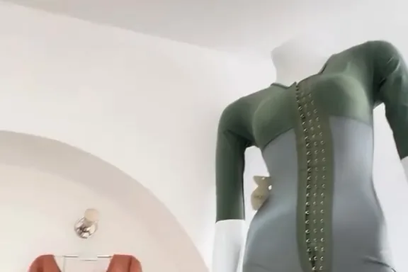 Une combinaison en powernet vert sauge sur un buste, sous l’arche de la boutique, sa colonne d’agrafes sur le devant